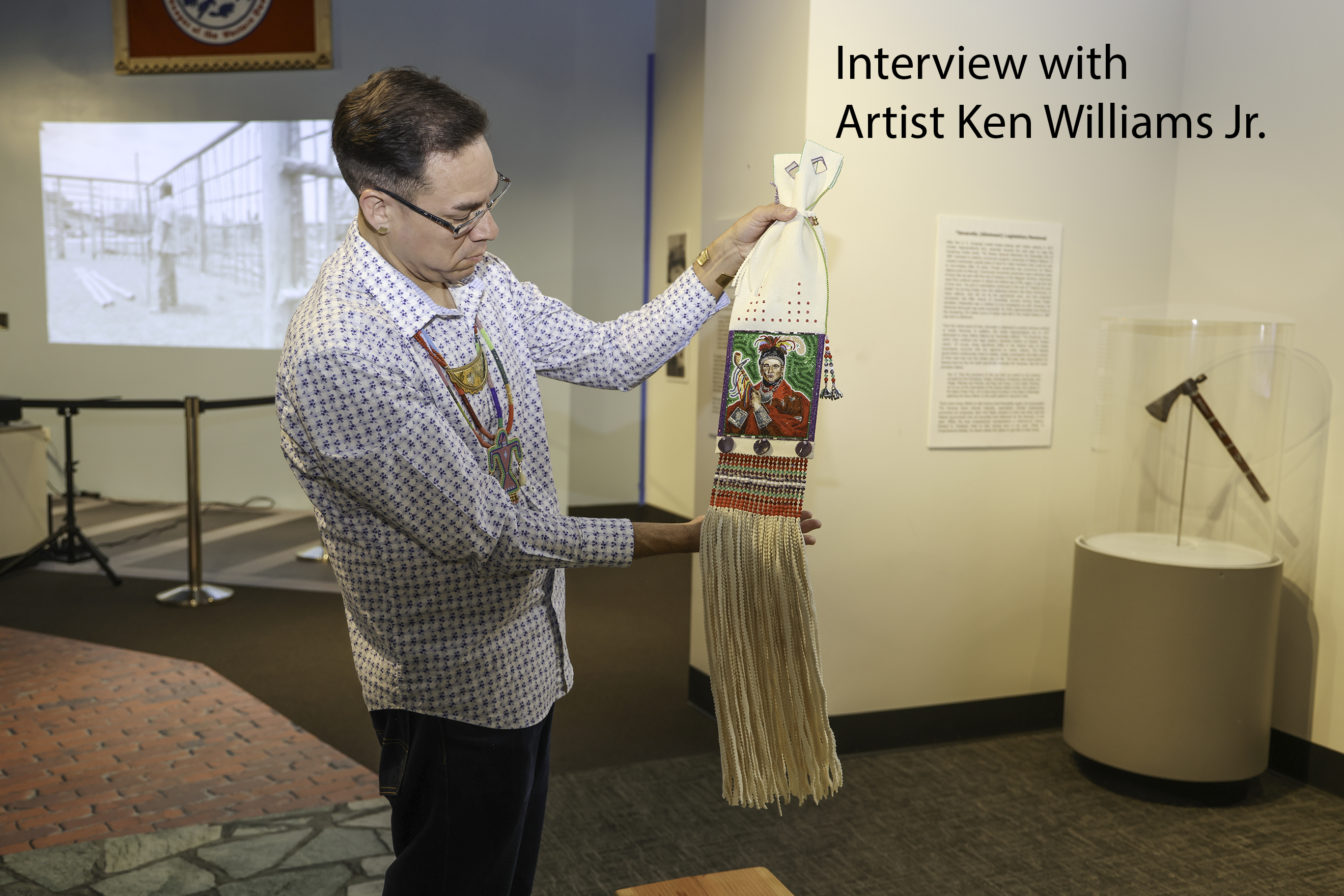 An artist holds up the Cornplanter bag which is a decorational bag adorned with beadwork that forms a potrait of Cornplanter.