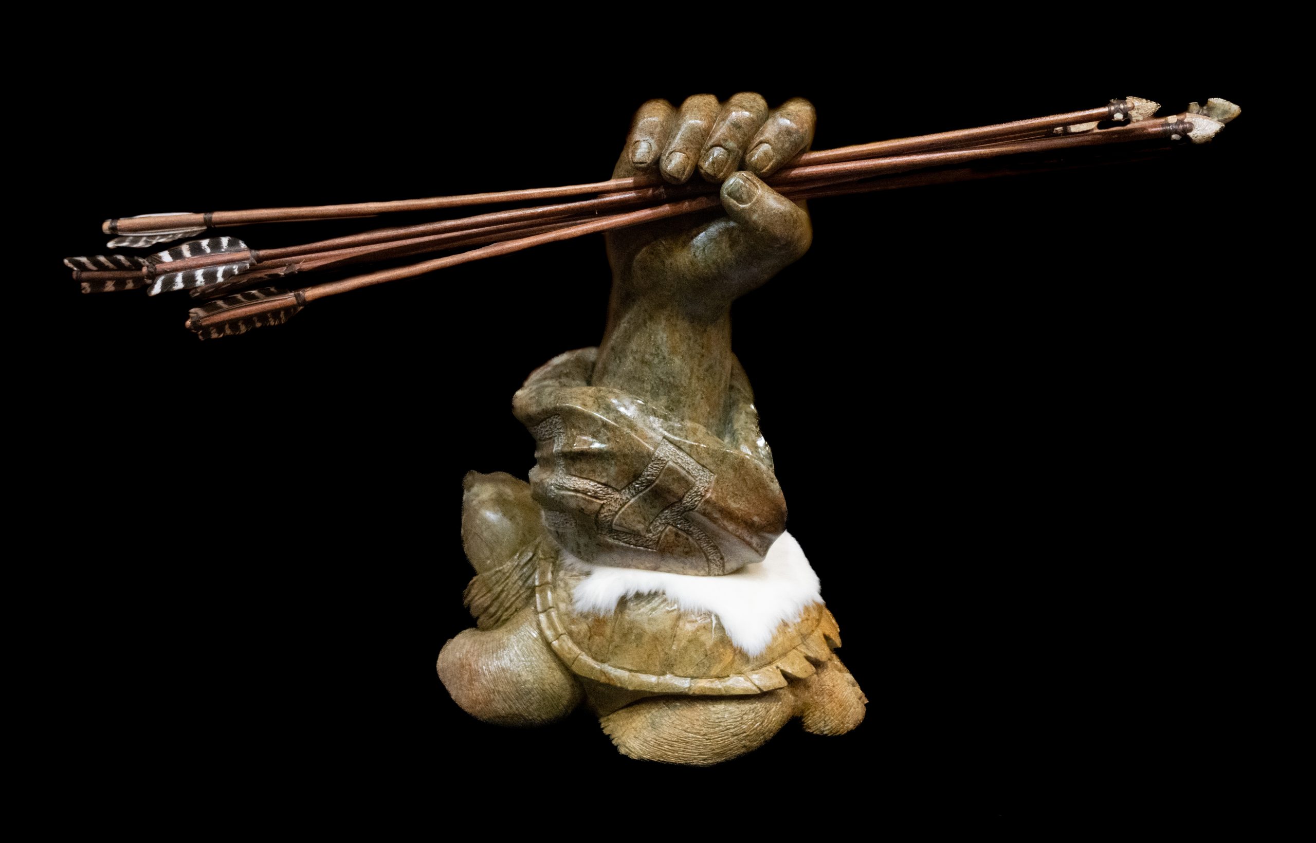 Sculpture of a turtle with half a human forearm rising out of its shell with the hand grasping a bundle of arrows.
